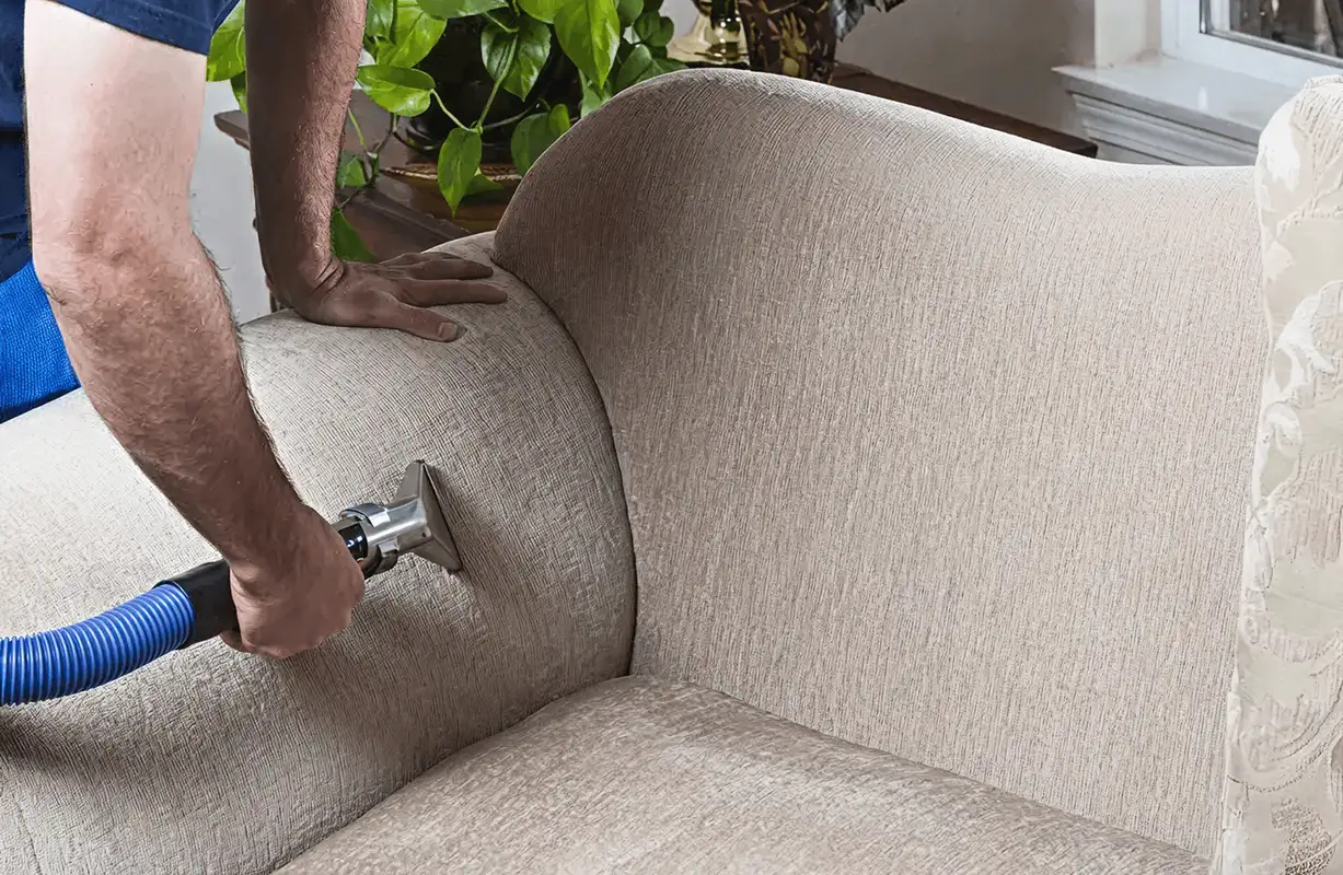 Professional upholstery cleaner deep-cleaning a fabric sofa with a handheld extraction tool and hose, West Palm Beach, FL.